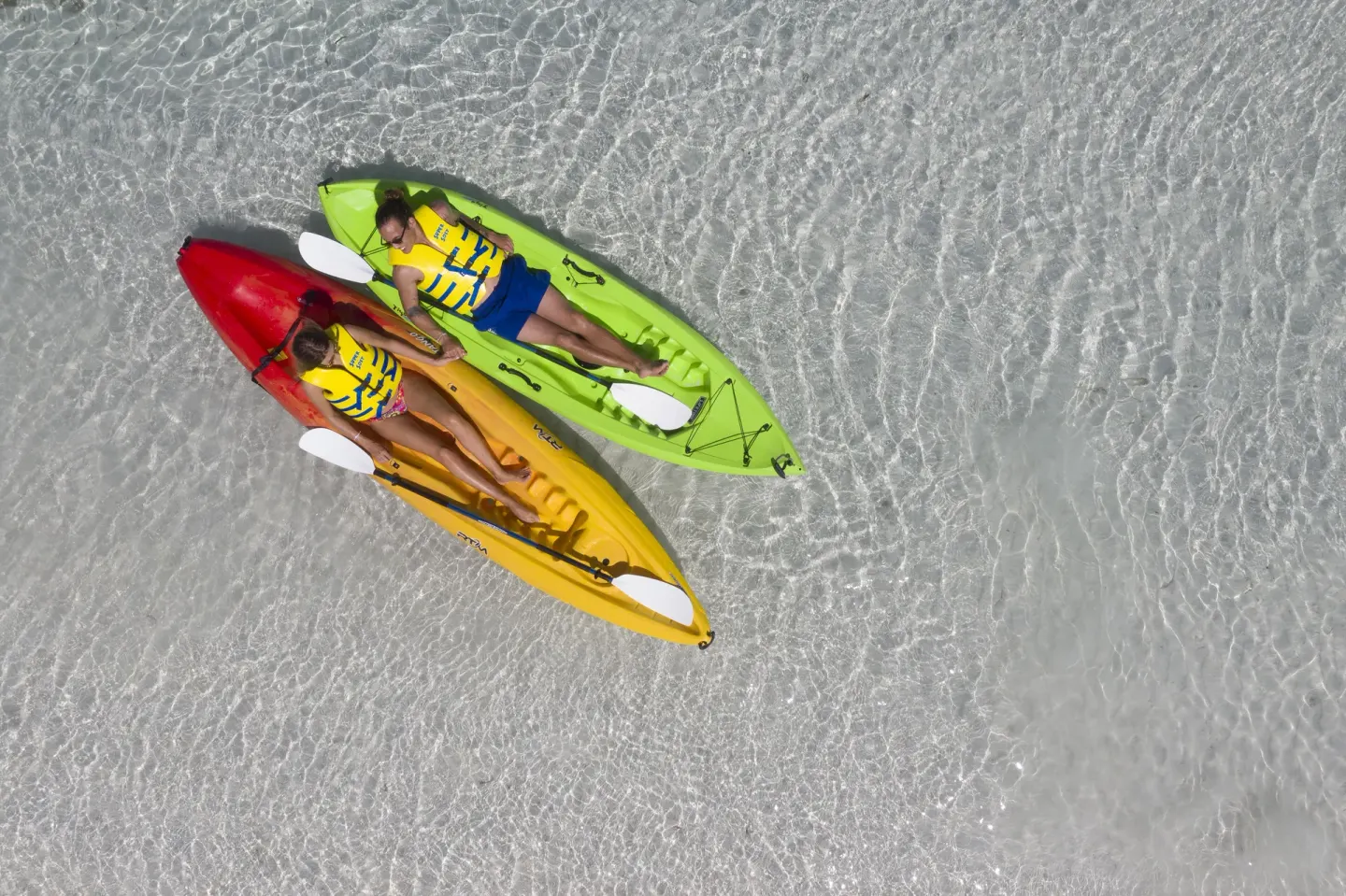 Two guests relax in colorful kayaks on clear shallow water at Ocean Eden Bay.