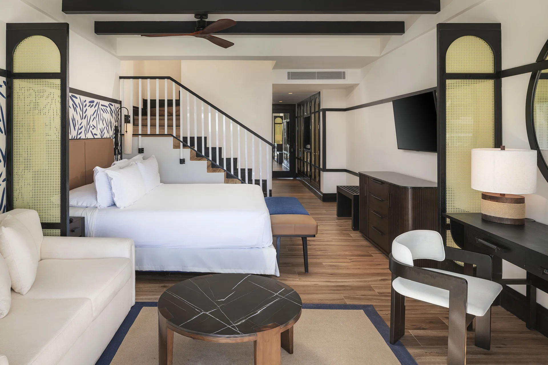 Loft-style guest room with king bed, sofa, desk, TV, and staircase at Ocean Eden Bay.