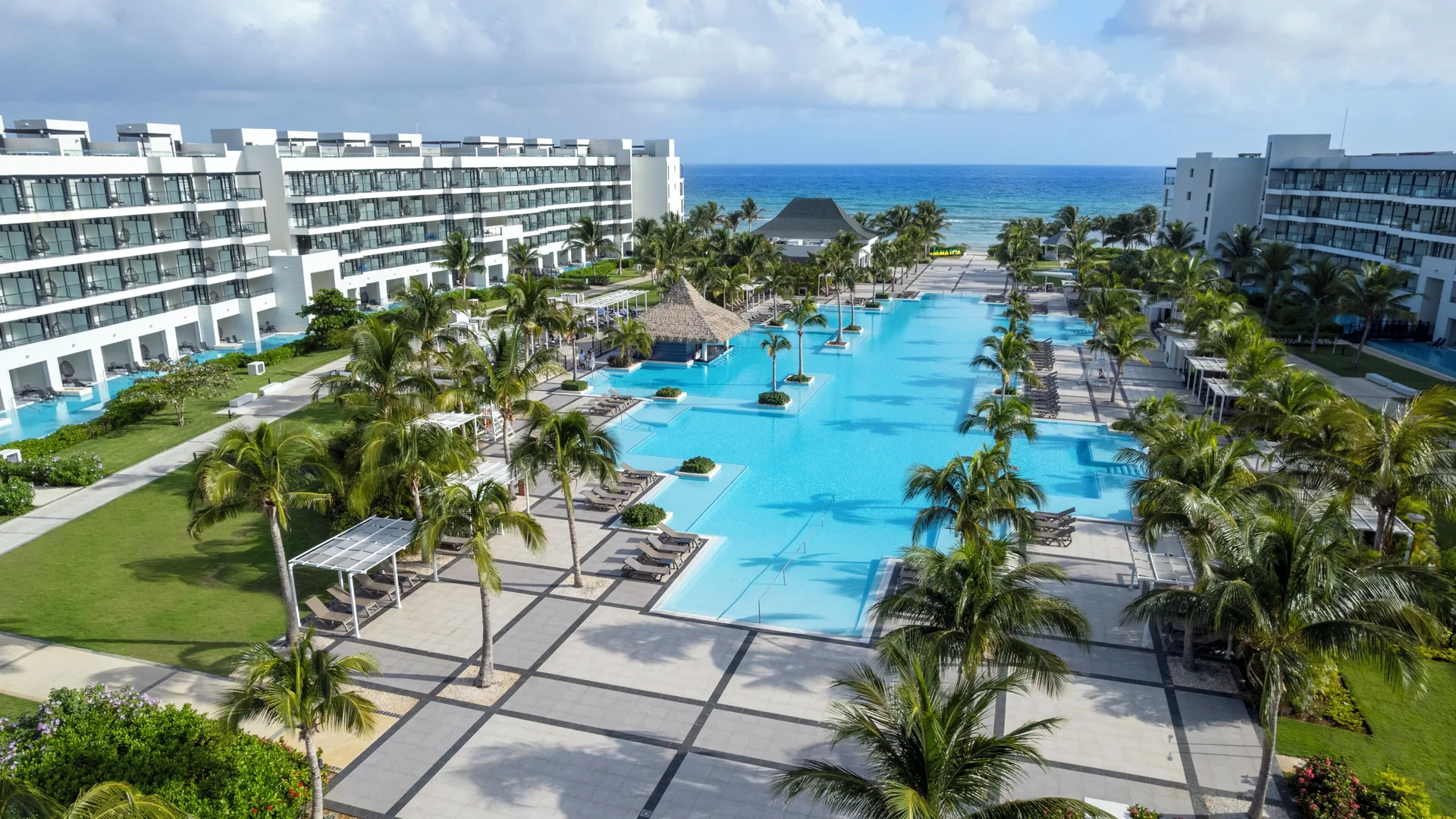 Aerial view of the main pool, palms, resort buildings, and ocean at Ocean Eden Bay.