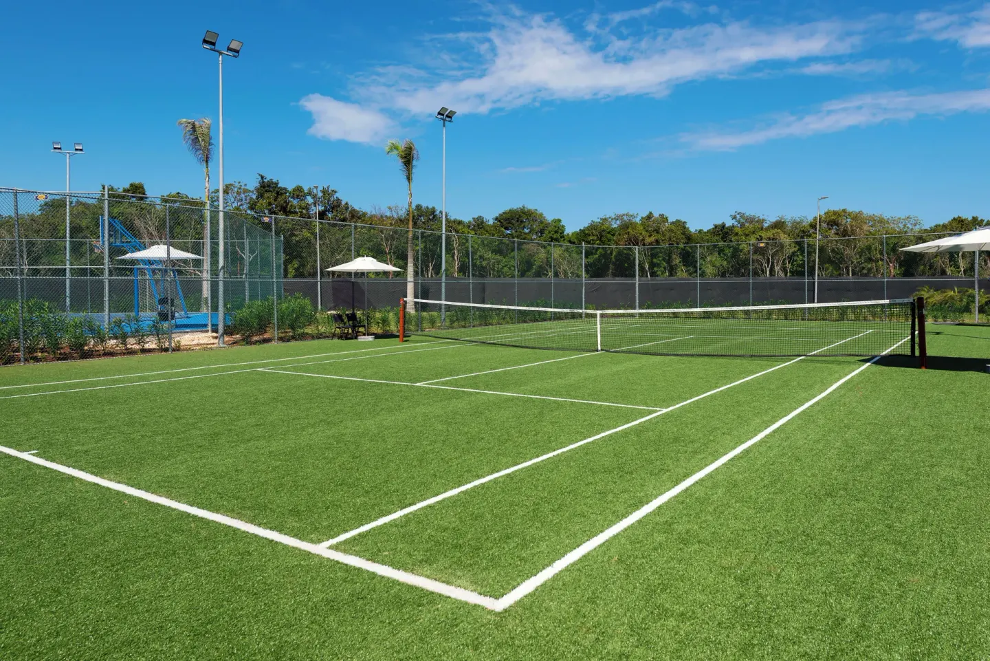 Outdoor tennis court with net, fencing, and light poles at Ocean Eden Bay.