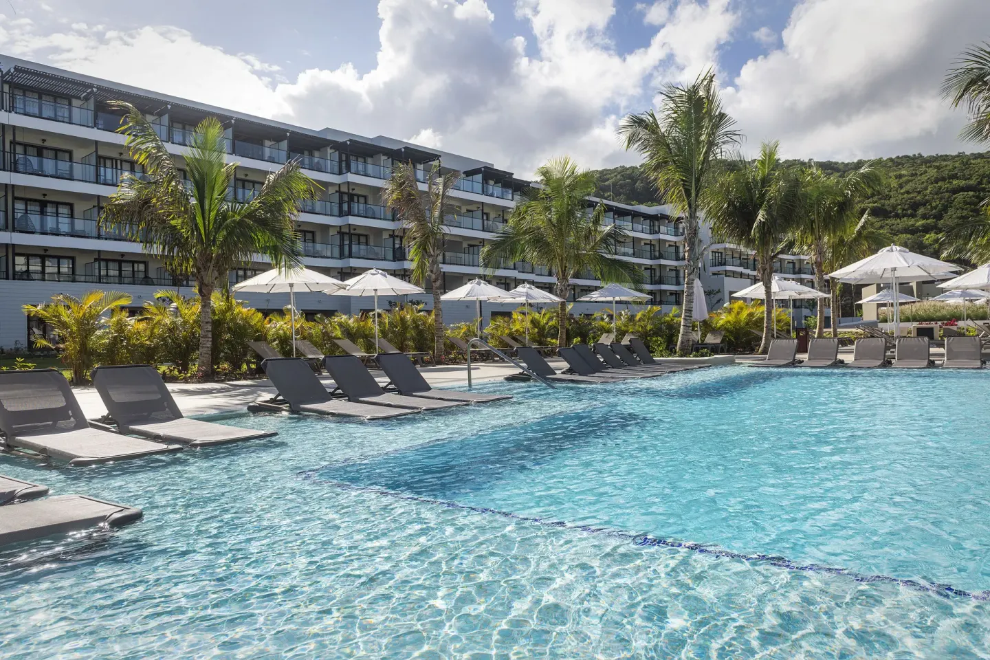Poolside loungers and umbrellas in front of guest buildings at Ocean Eden Bay.