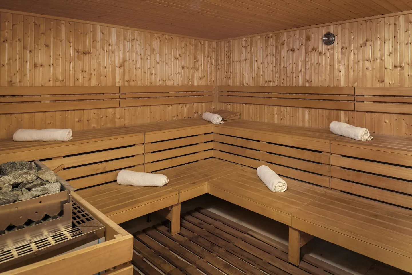 Wood sauna with tiered benches, rolled towels, and heater stones at Ocean Eden Bay.