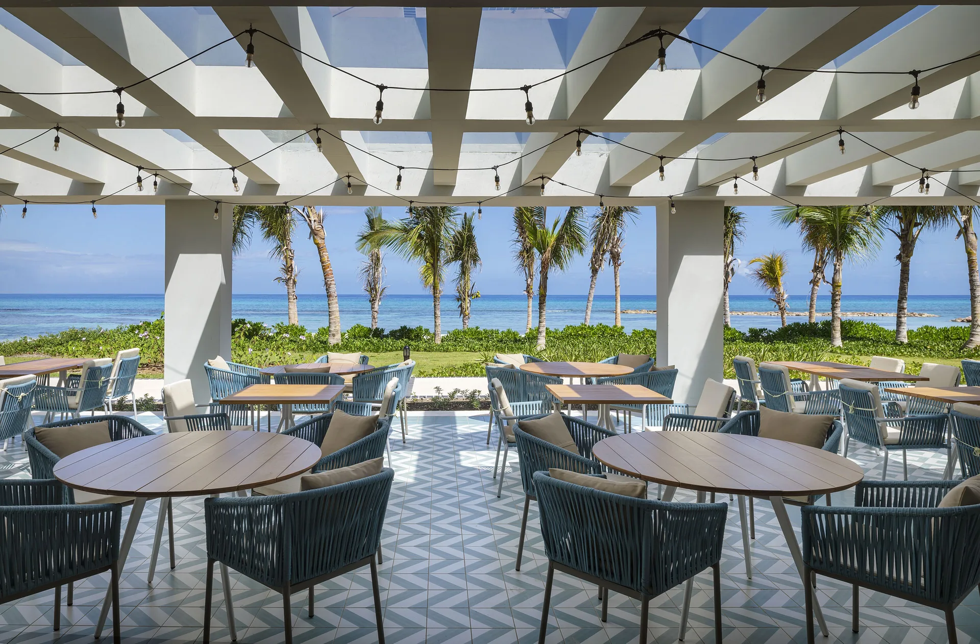 Oceanfront terrace with round tables and palm views at Ocean Eden Bay.