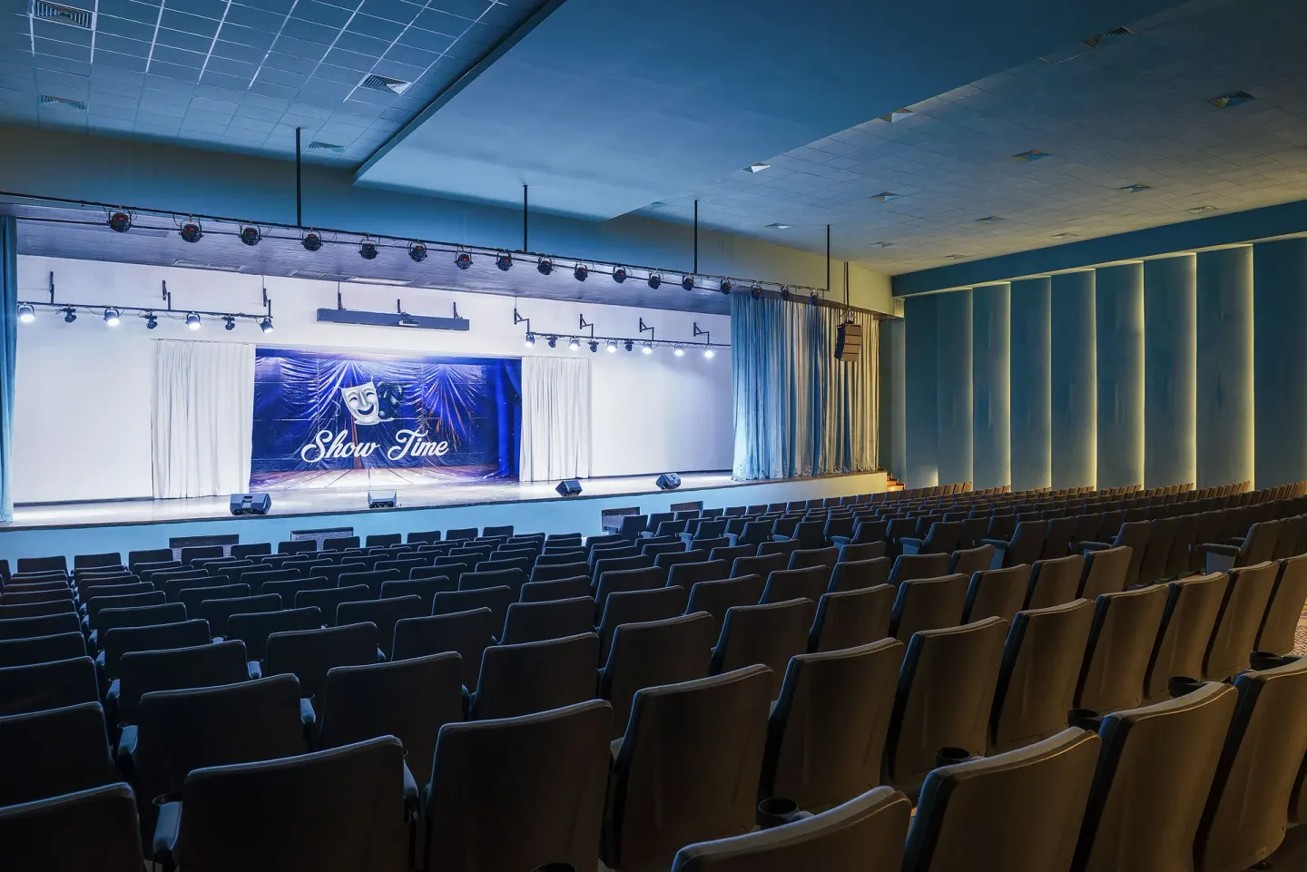 Empty auditorium with rows of seats and a lit stage at Ocean El Faro Resort.