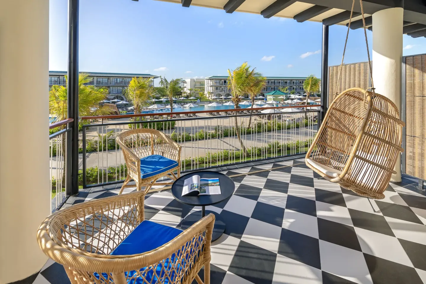 Balcony at Ocean El Faro Resort with wicker chairs, a hanging chair, and pool views.