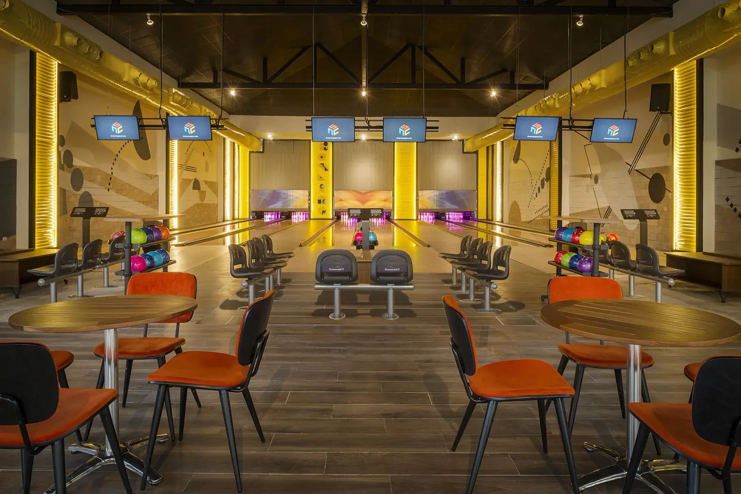Empty bowling alley with tables, orange chairs, and ball racks at Ocean El Faro Resort.