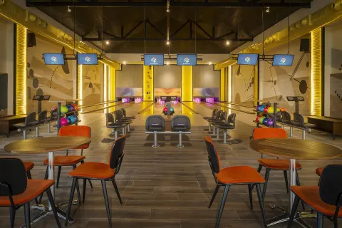 Empty bowling alley with tables, orange chairs, and ball racks at Ocean El Faro Resort.