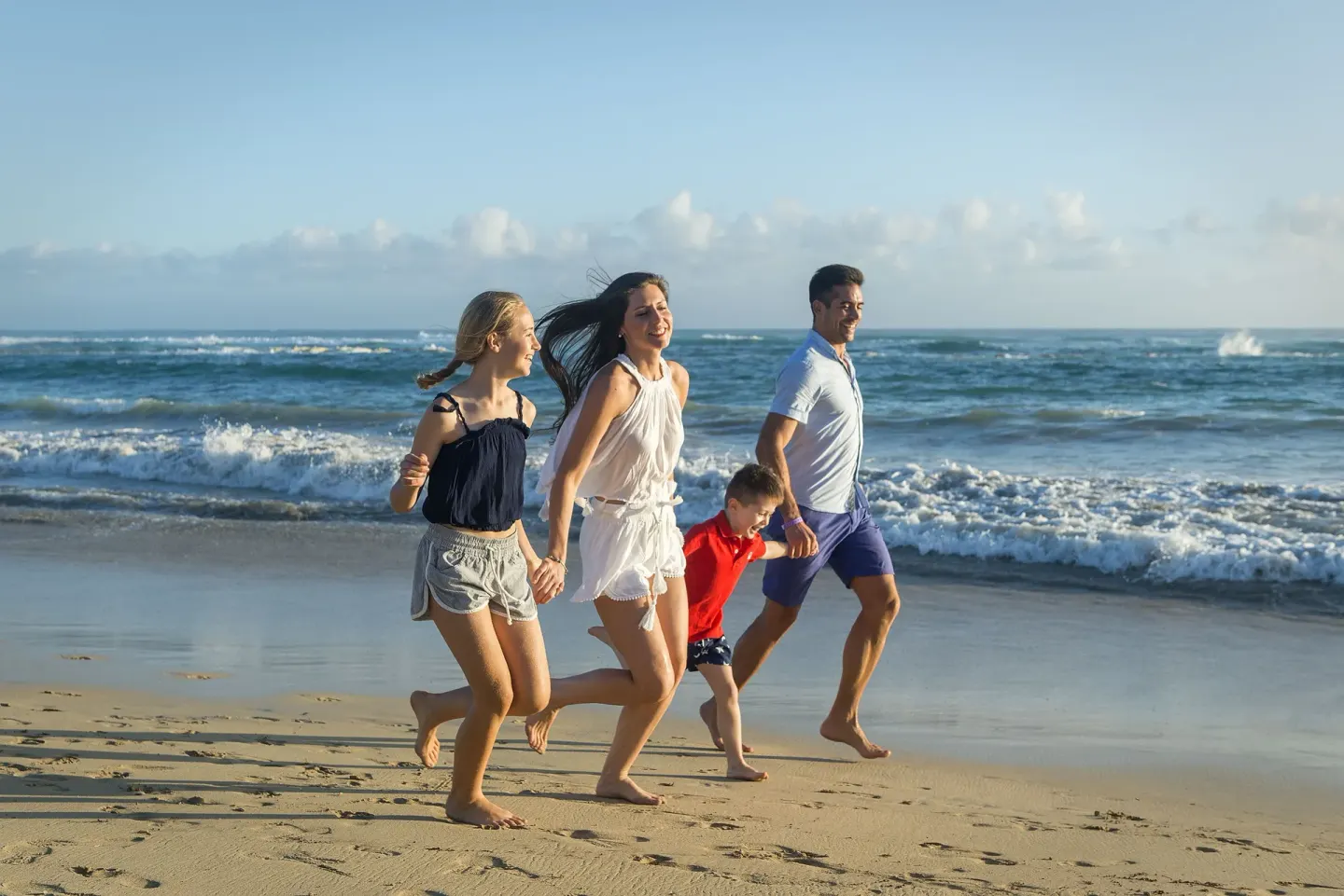 Family running along the ocean shoreline at Ocean El Faro Resort.