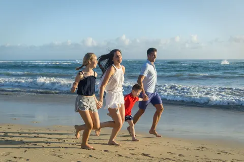 Family running along the ocean shoreline at Ocean El Faro Resort.