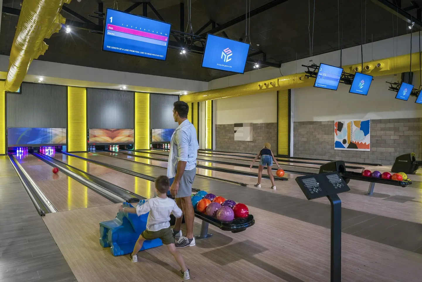 Family bowling lanes with score screens and colorful balls at Ocean El Faro Resort.