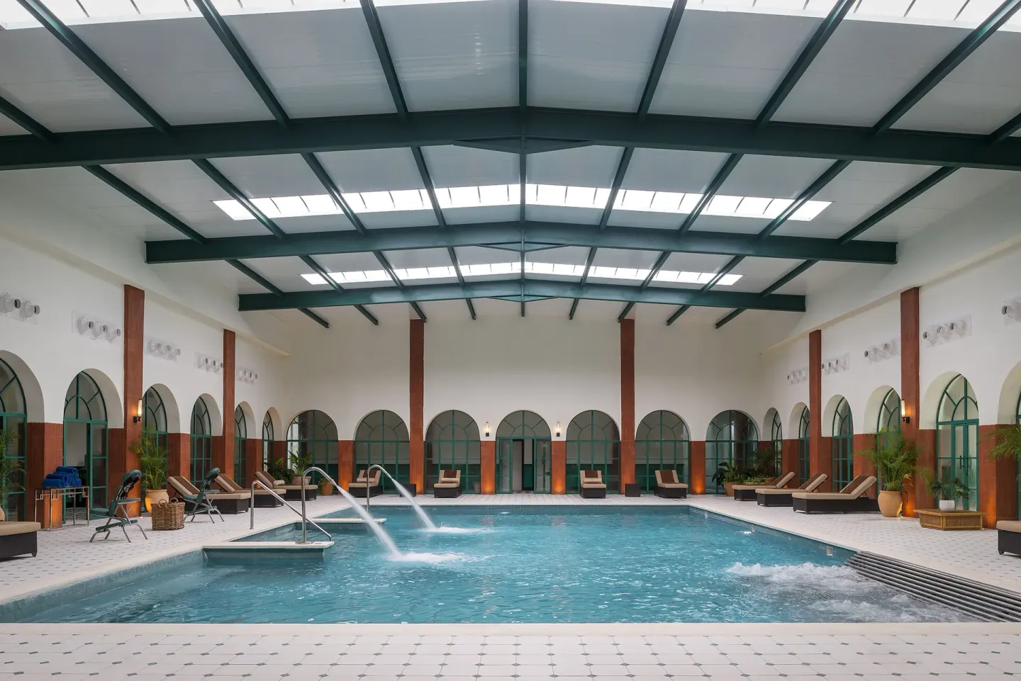Indoor pool with loungers, arched windows, and water jets at Ocean El Faro Resort.