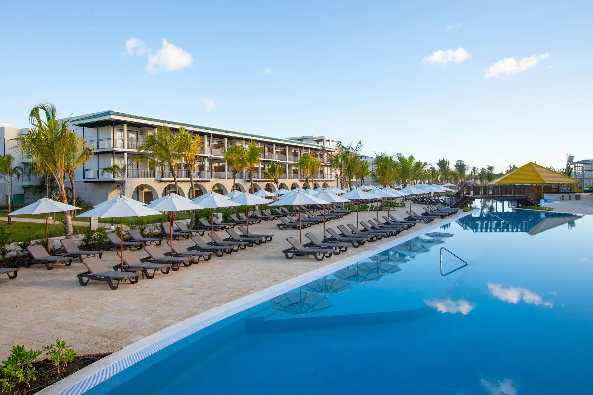 Pool deck with rows of loungers and white umbrellas at Ocean El Faro Resort.