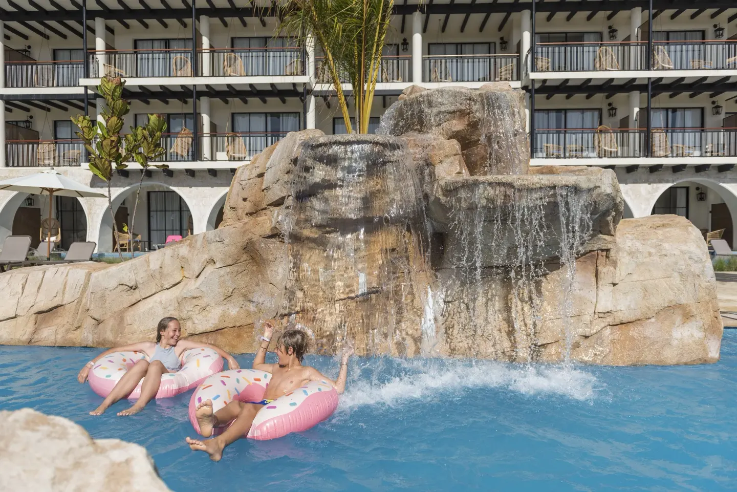 Guests floating in a pool beneath a rock waterfall at Ocean El Faro Resort.