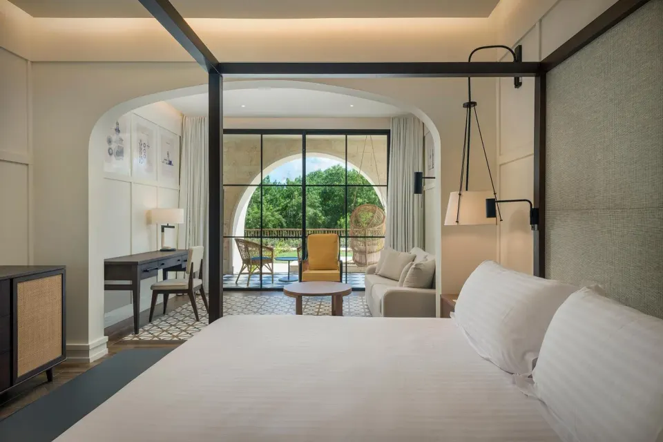 Junior Suite Nature View king bed at Ocean El Faro Resort facing a sofa and leafy balcony.