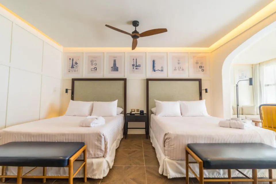 Two beds in a Junior Suite Nature View guest room at Ocean El Faro Resort with benches and ceiling fan.