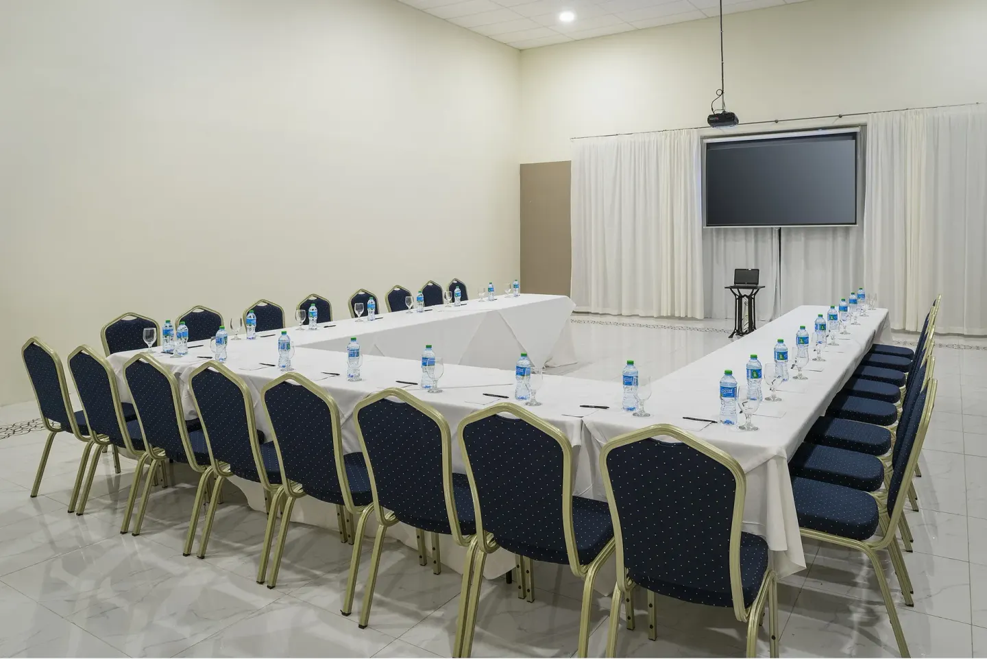 Meeting room with U-shaped tables, chairs, water bottles, and screen at Ocean El Faro Resort.