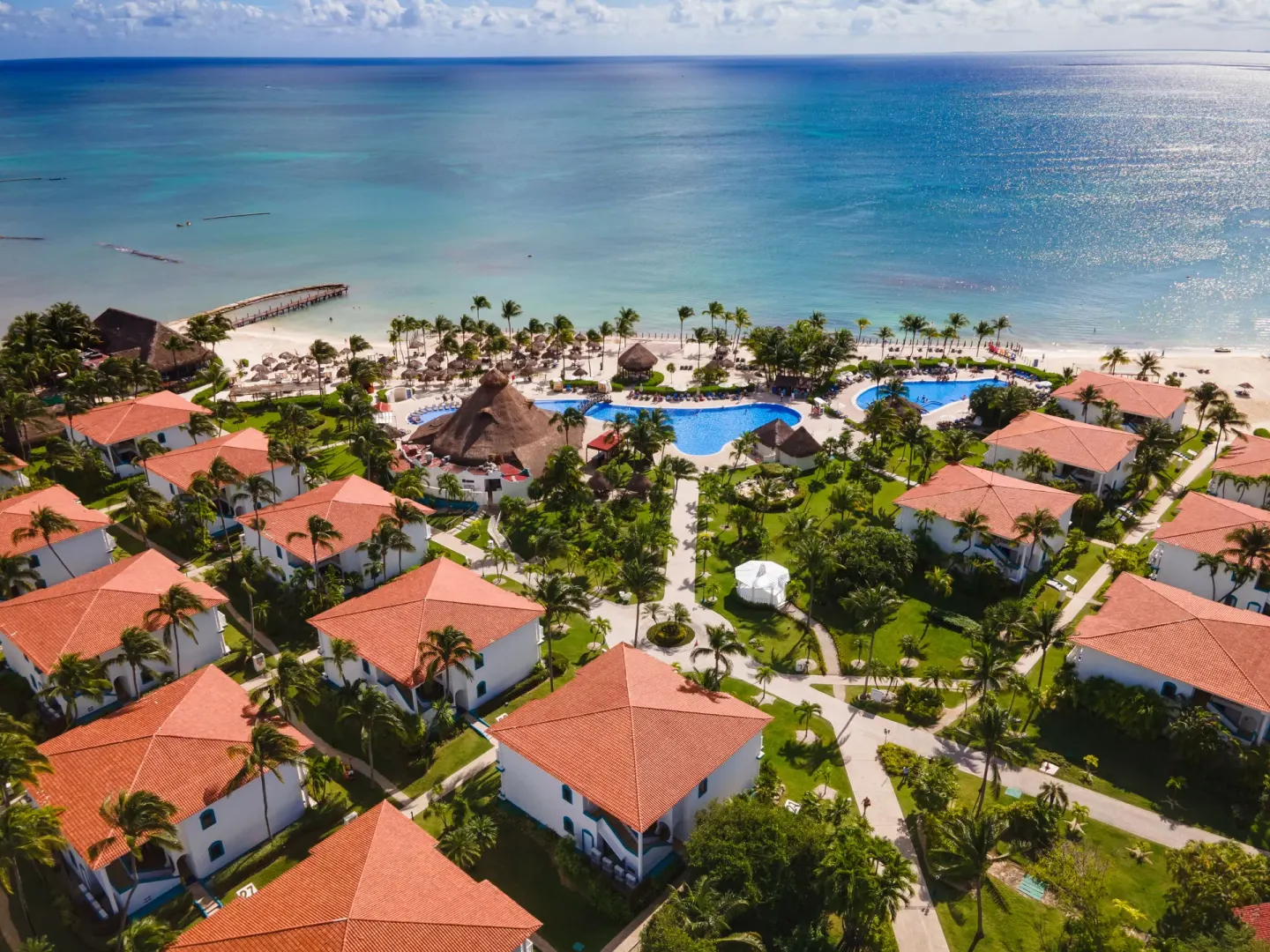 Aerial view of beachfront pools, gardens, and red-roofed buildings at Ocean Maya Royale.
