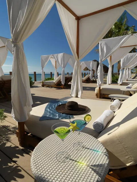 Beach cabanas with loungers, towels, and drinks by the ocean at Ocean Maya Royale.