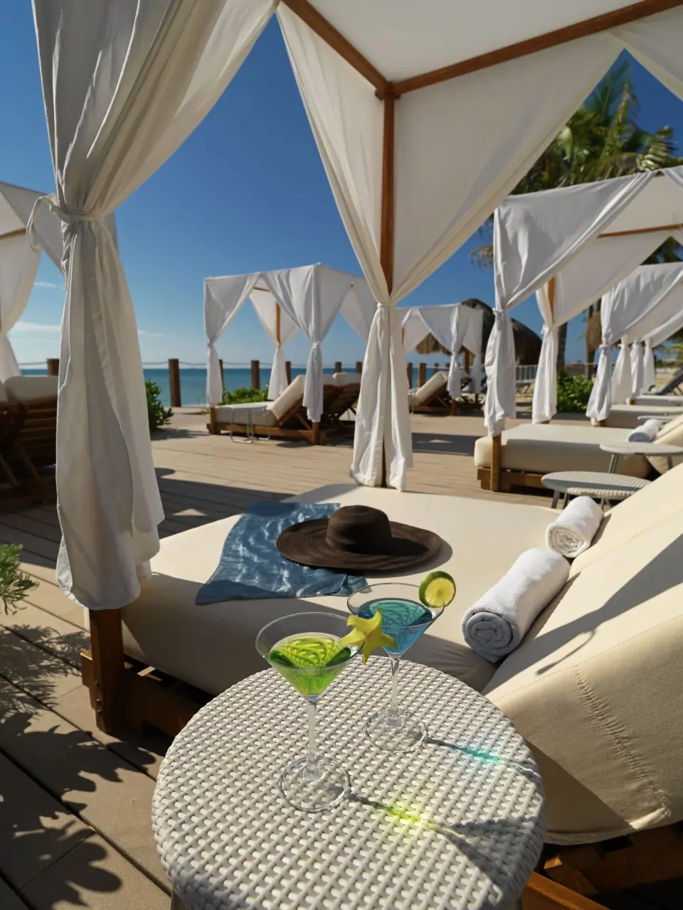 Beach cabanas with loungers, towels, and drinks by the ocean at Ocean Maya Royale.