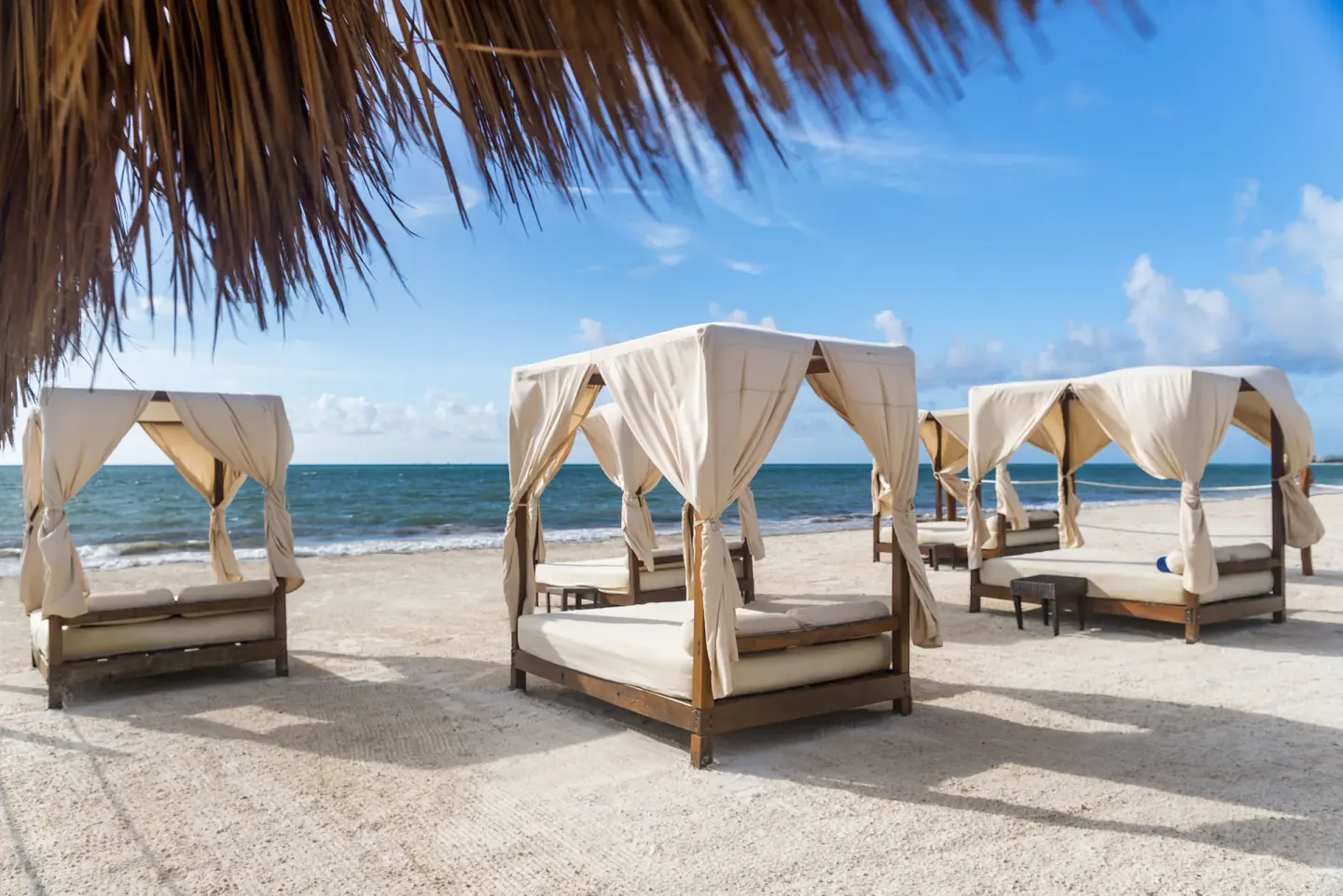 Curtained daybeds sit on the sand beside the sea at Ocean Maya Royale.