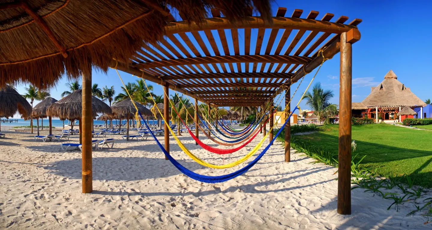 Colorful hammocks hang beneath a wooden pergola by the beach at Ocean Maya Royale.