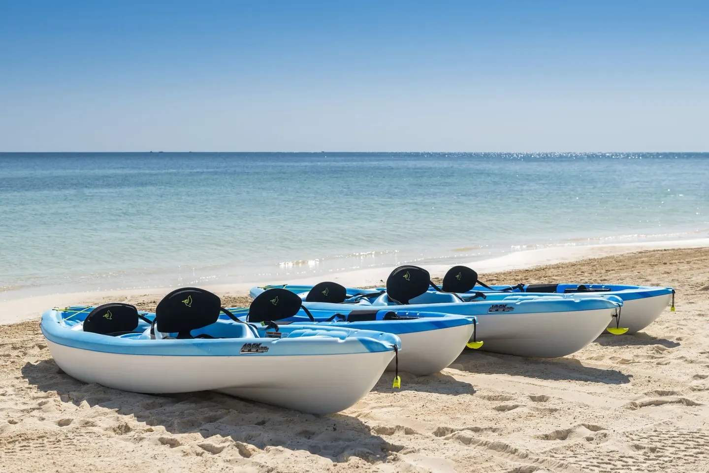 Blue kayaks lined on the sand beside the sea at Ocean Maya Royale.