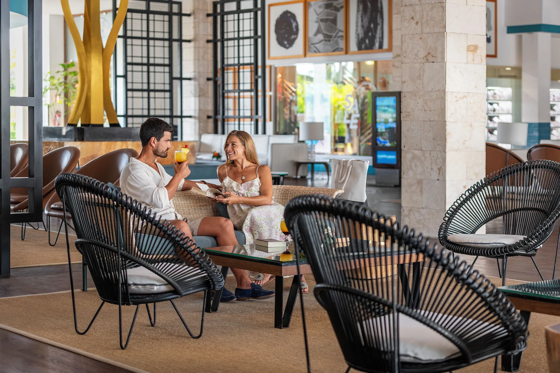 Couple seated with drinks in a woven-chair lobby lounge at Ocean Maya Royale.