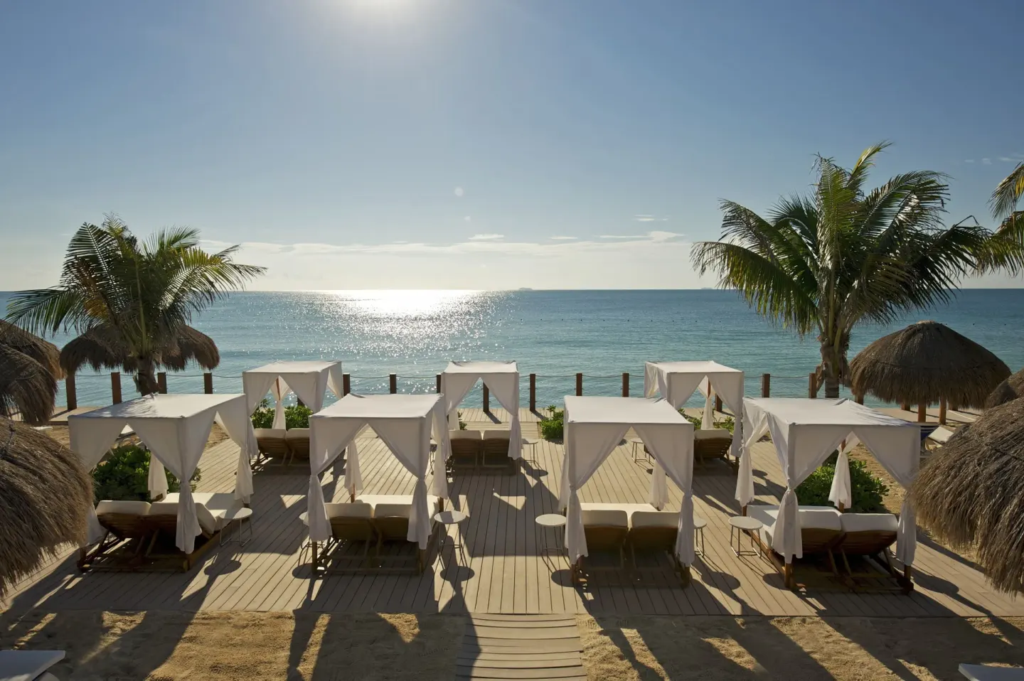 White cabana beds overlook the sunlit ocean at Ocean Maya Royale.