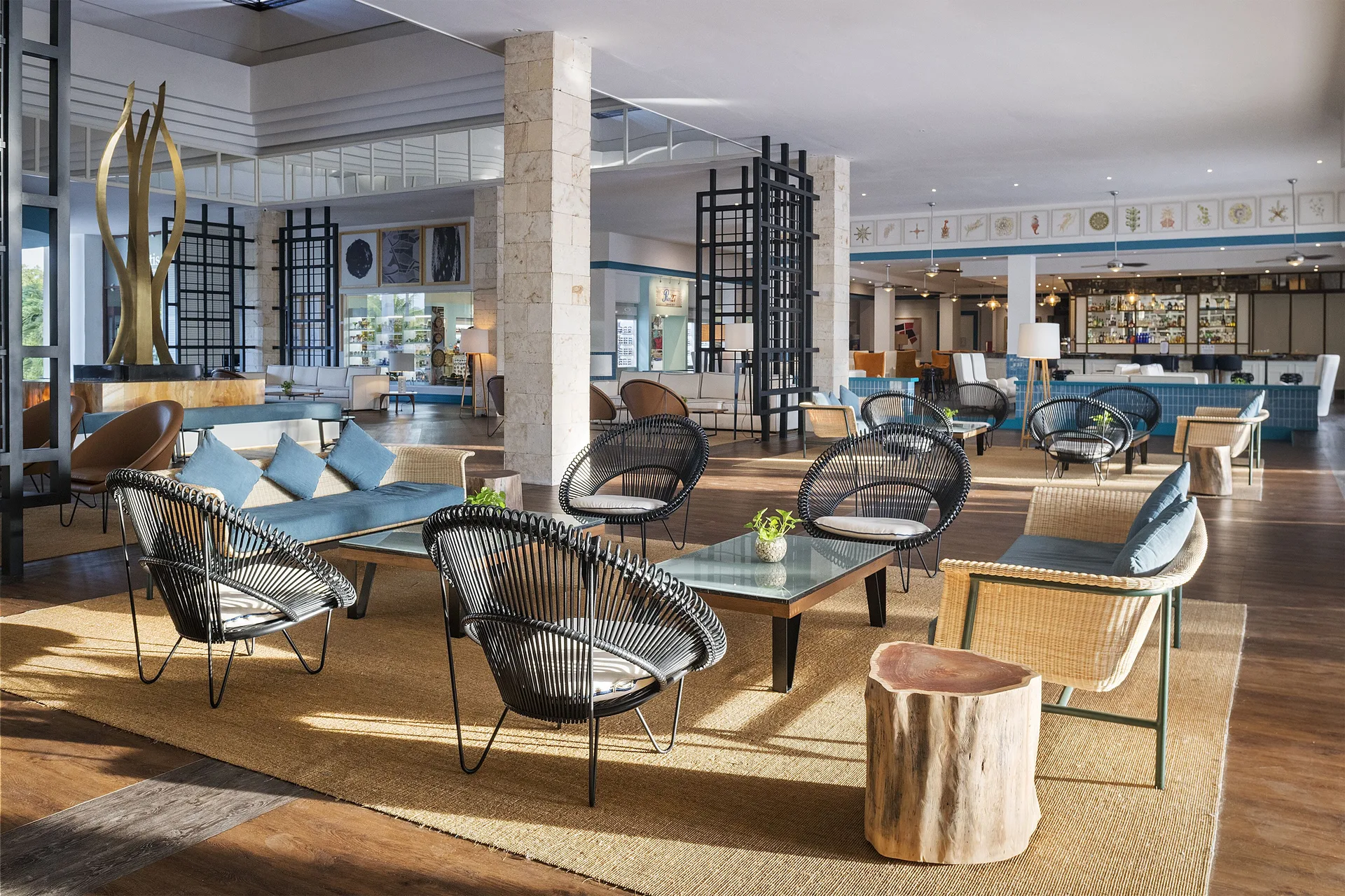 Open lobby lounge with woven chairs, sofas, tables, and a bar at Ocean Maya Royale.