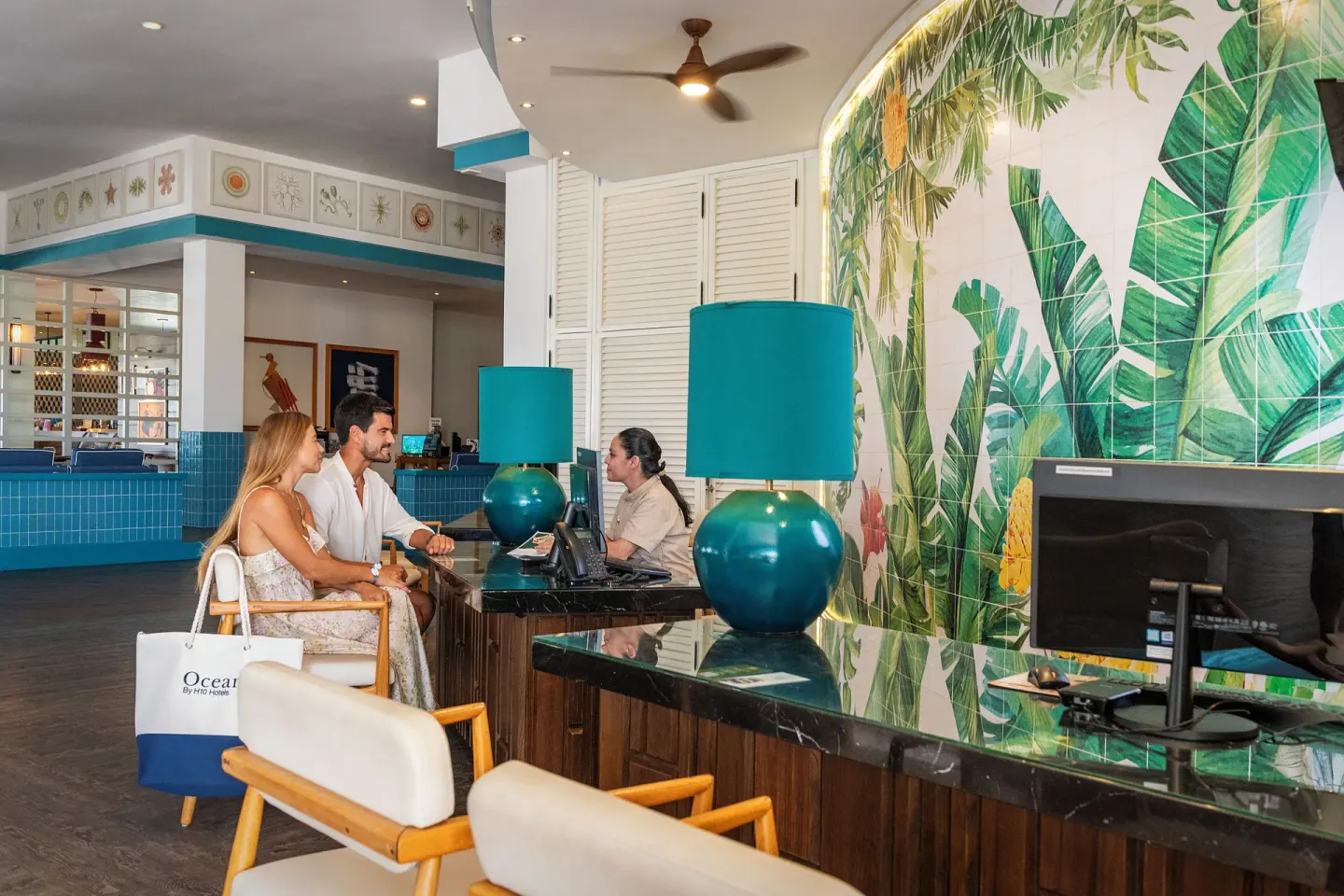 Reception desks with turquoise lamps and a tropical wall mural at Ocean Maya Royale.