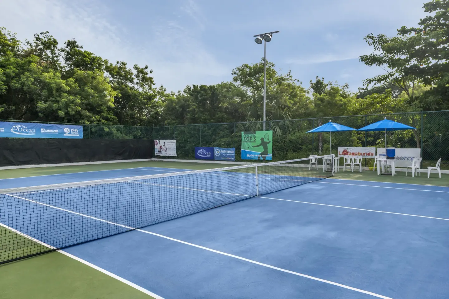 Tennis court with seating and blue umbrellas at Ocean Maya Royale.