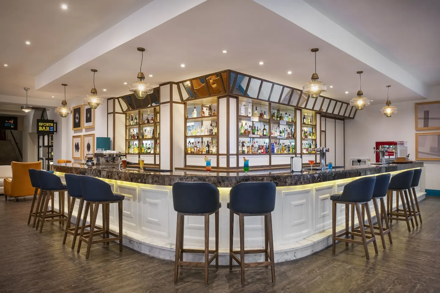 Lobby Bar counter with stools, cocktails, and backlit shelves at Ocean Maya Royale.