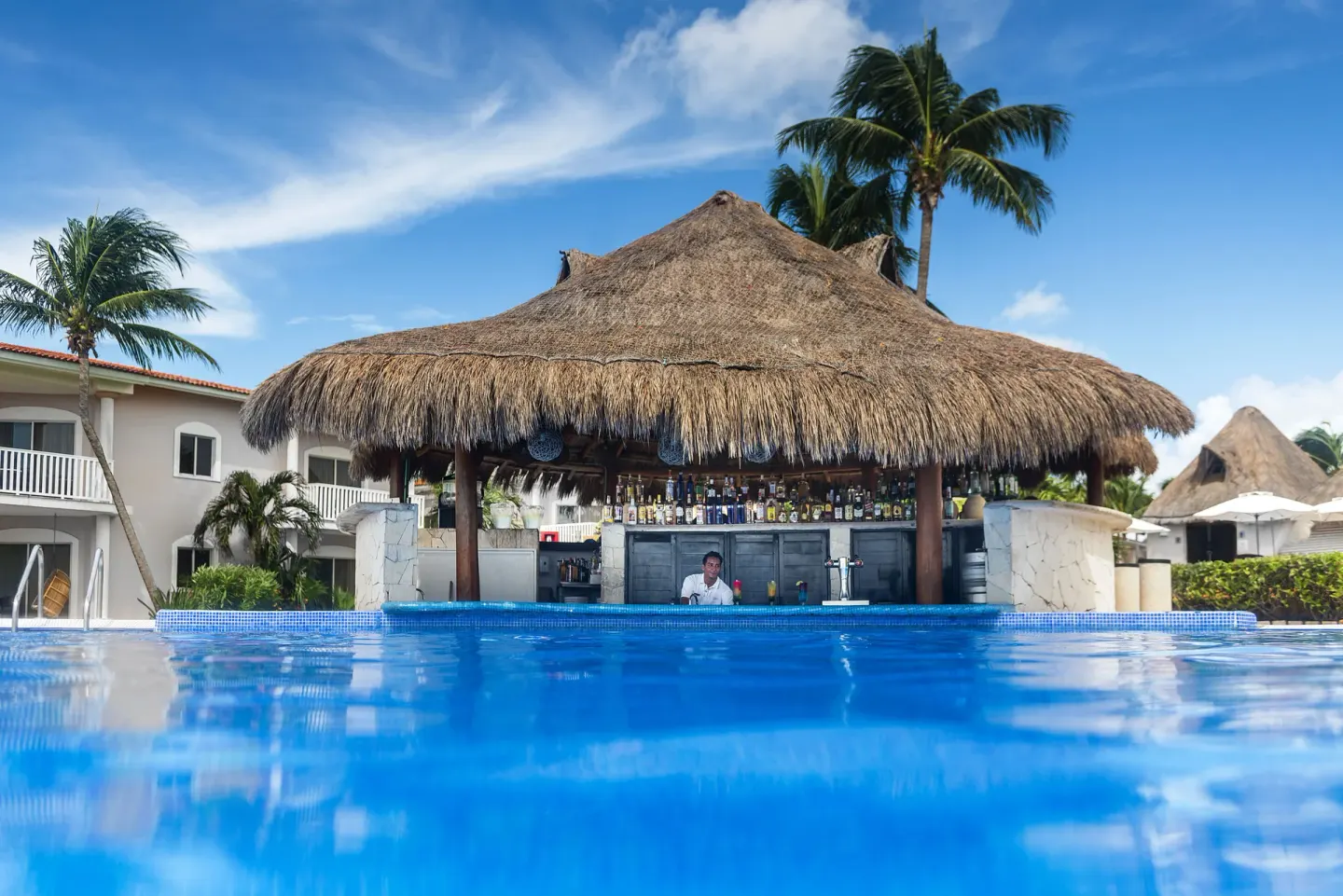 Thatched swim-up pool bar beside bright blue water at Ocean Maya Royale.
