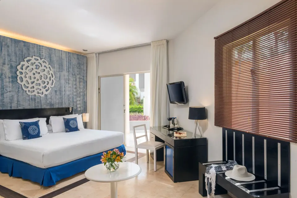 Junior Suite Nature View king bed with desk and patio door at Ocean Maya Royale.