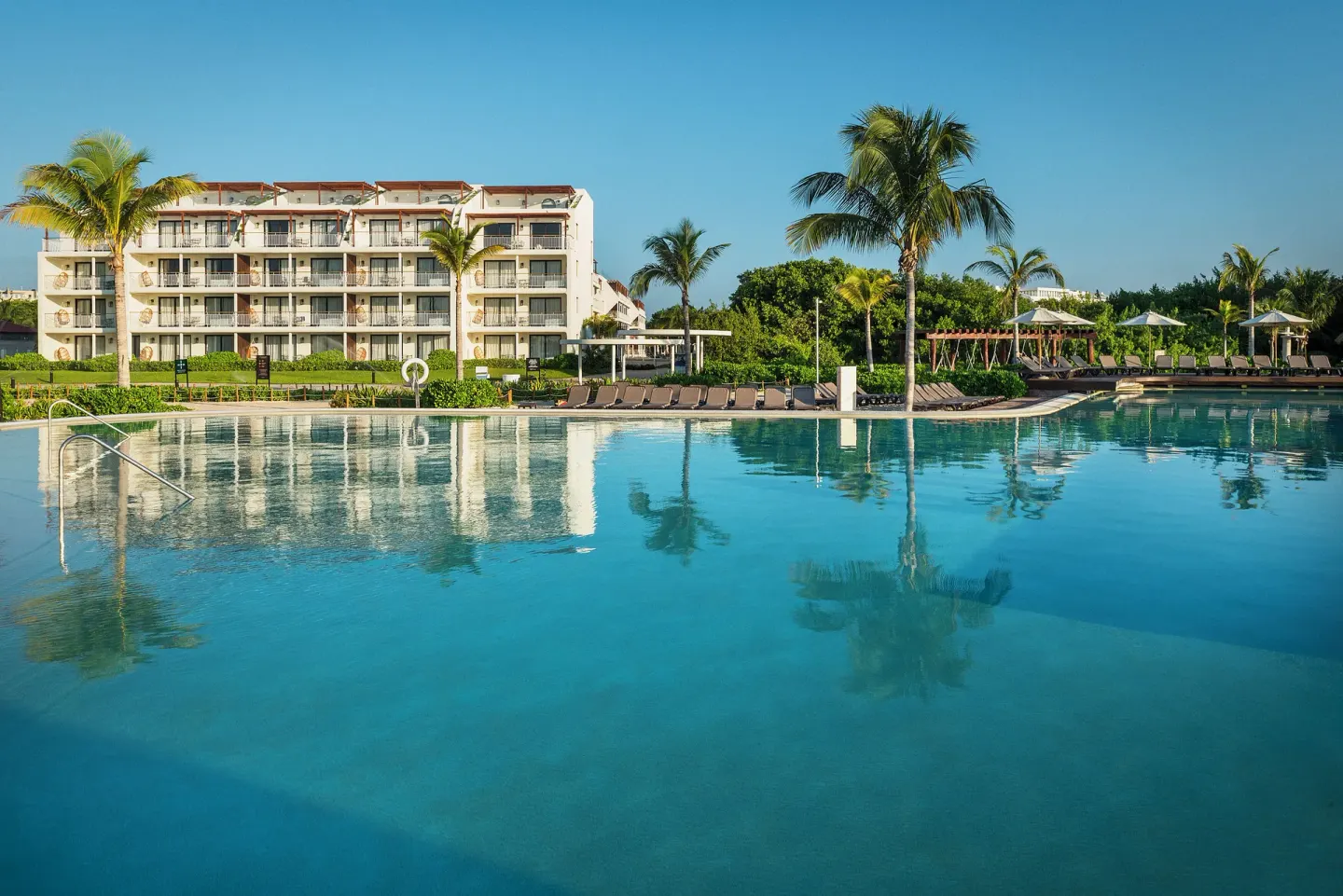 Large resort pool with palm trees, loungers, and guest building at Ocean Riviera Paradise.