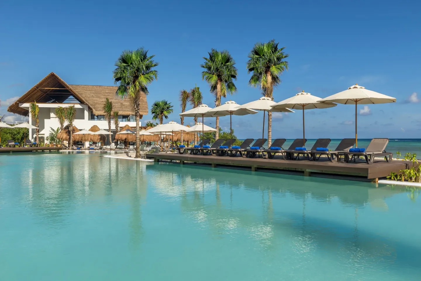 Pool deck with loungers, umbrellas, palms, and ocean beyond at Ocean Riviera Paradise.
