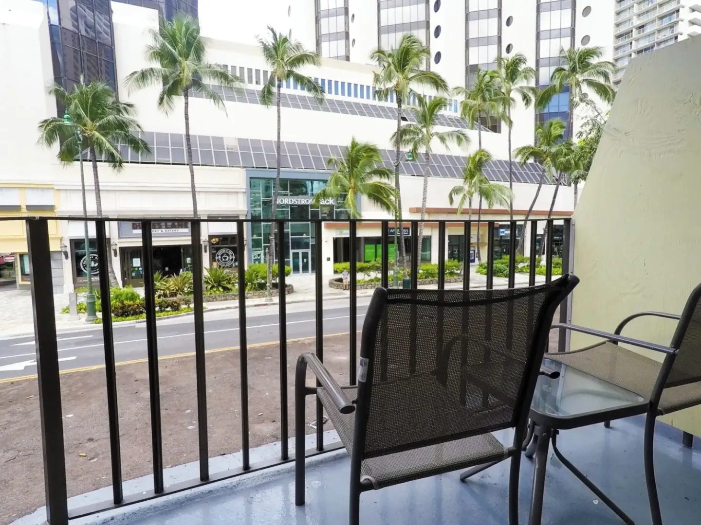 Balcony chairs overlook a palm-lined street at Ohia Waikiki Studio Suites.