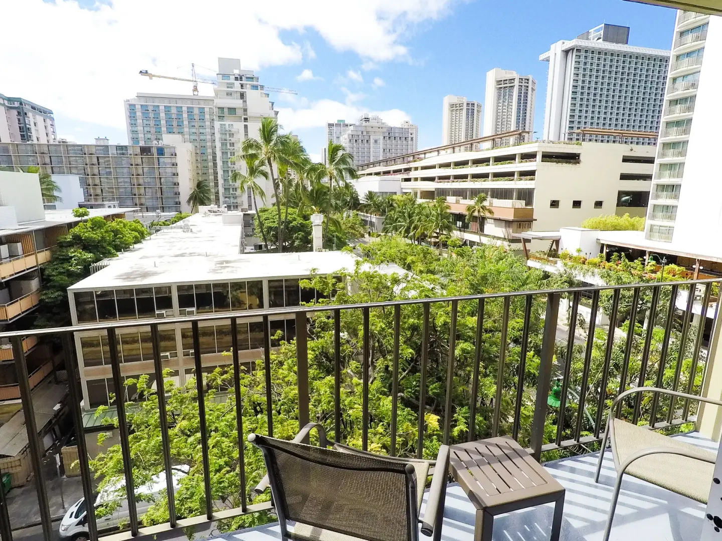 Balcony seating faces treetops and Waikiki buildings at Ohia Waikiki Studio Suites.