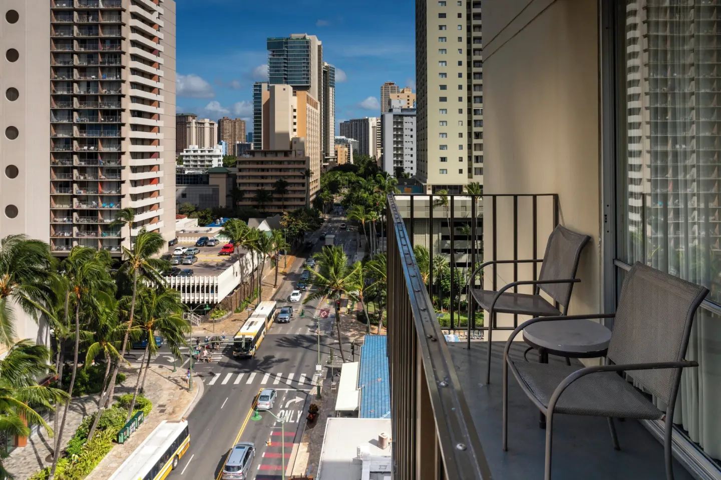 Balcony table and chairs overlook a busy Waikiki street at Ohia Waikiki Studio Suites.