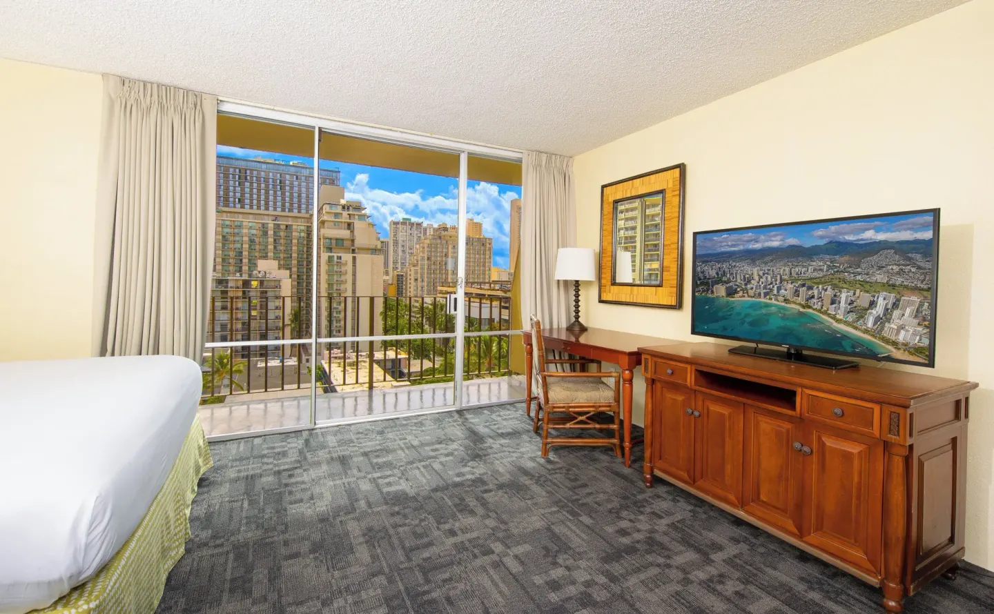 Guest room with bed, dresser, desk and balcony windows at Ohia Waikiki Studio Suites.