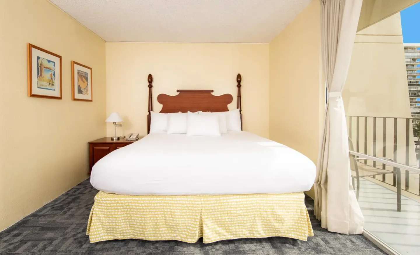 Guest room bed beside sliding balcony doors at Ohia Waikiki Studio Suites.