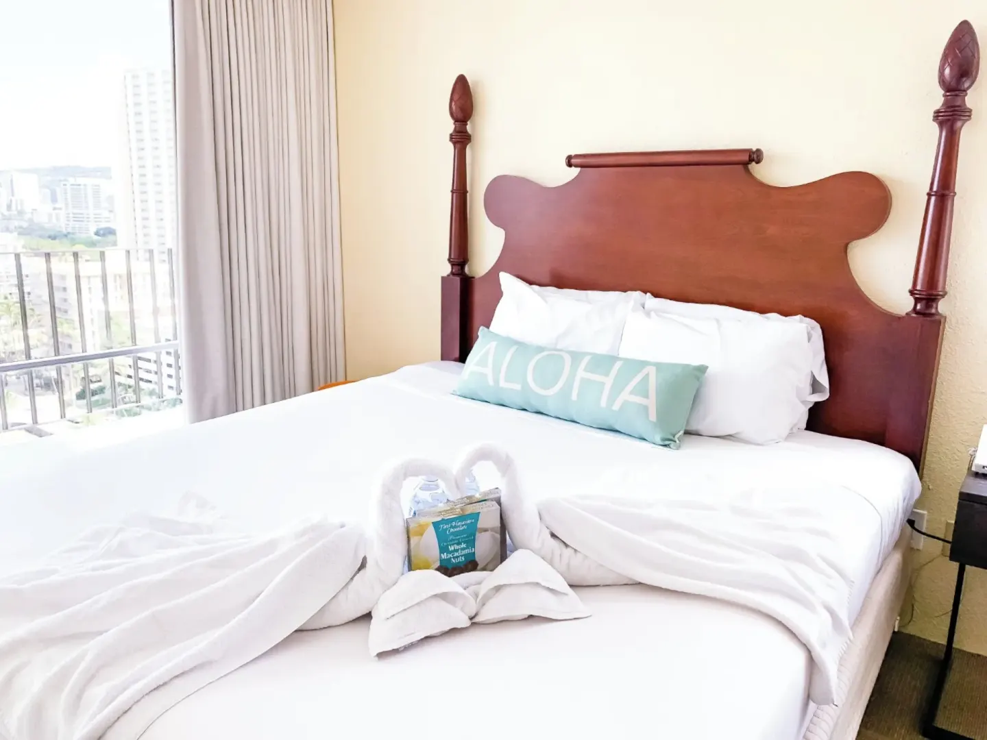 Guest room bed with white linens and balcony beside it at Ohia Waikiki Studio Suites.