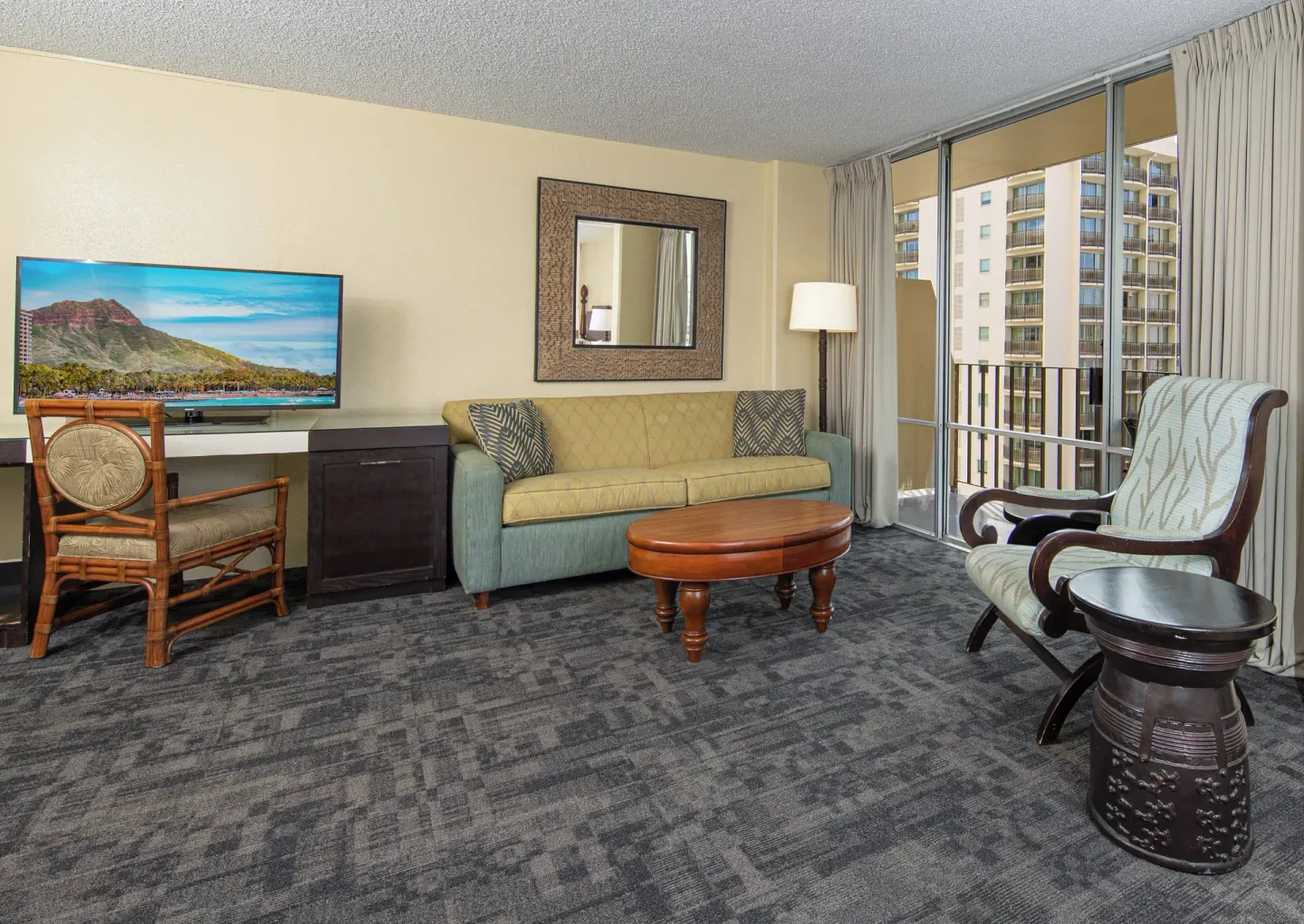 Sitting area with sofa, armchair, TV and balcony doors at Ohia Waikiki Studio Suites.