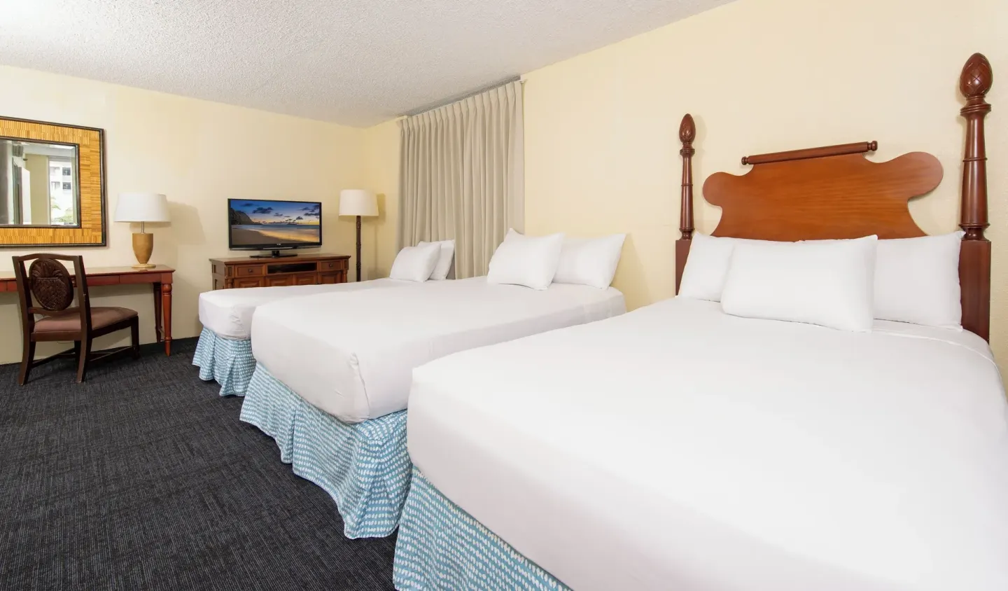 Three white beds with wood headboards in a guest room at Ohia Waikiki Studio Suites.