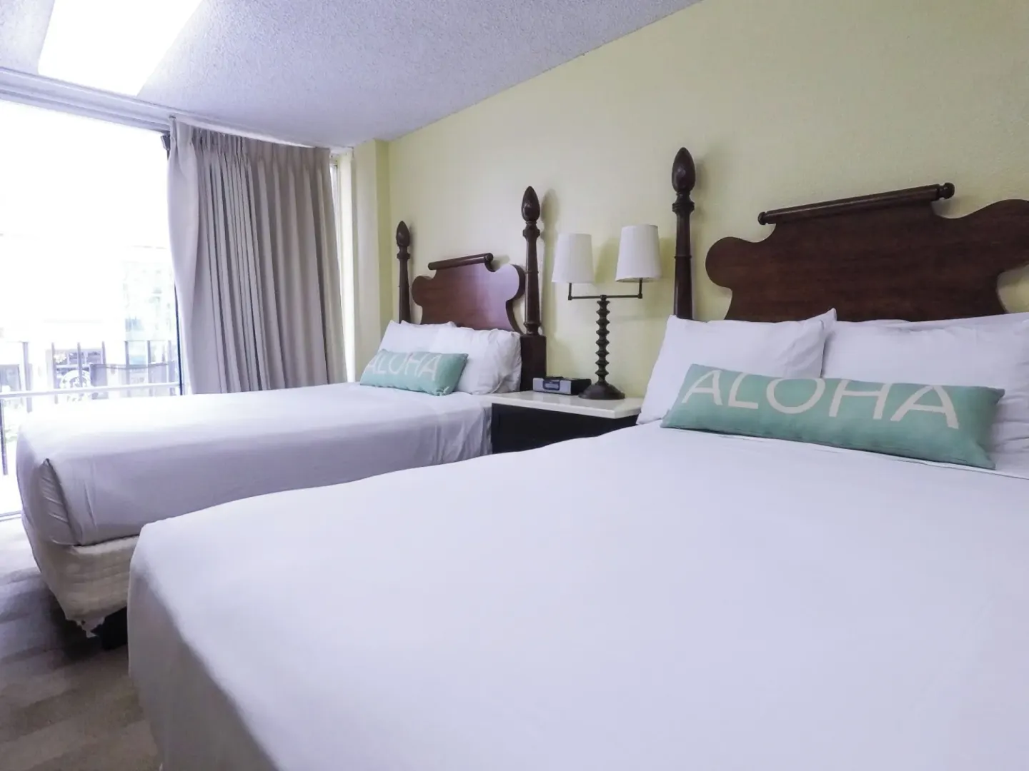 Guest room with two beds, white linens, and balcony curtains at Ohia Waikiki Studio Suites.