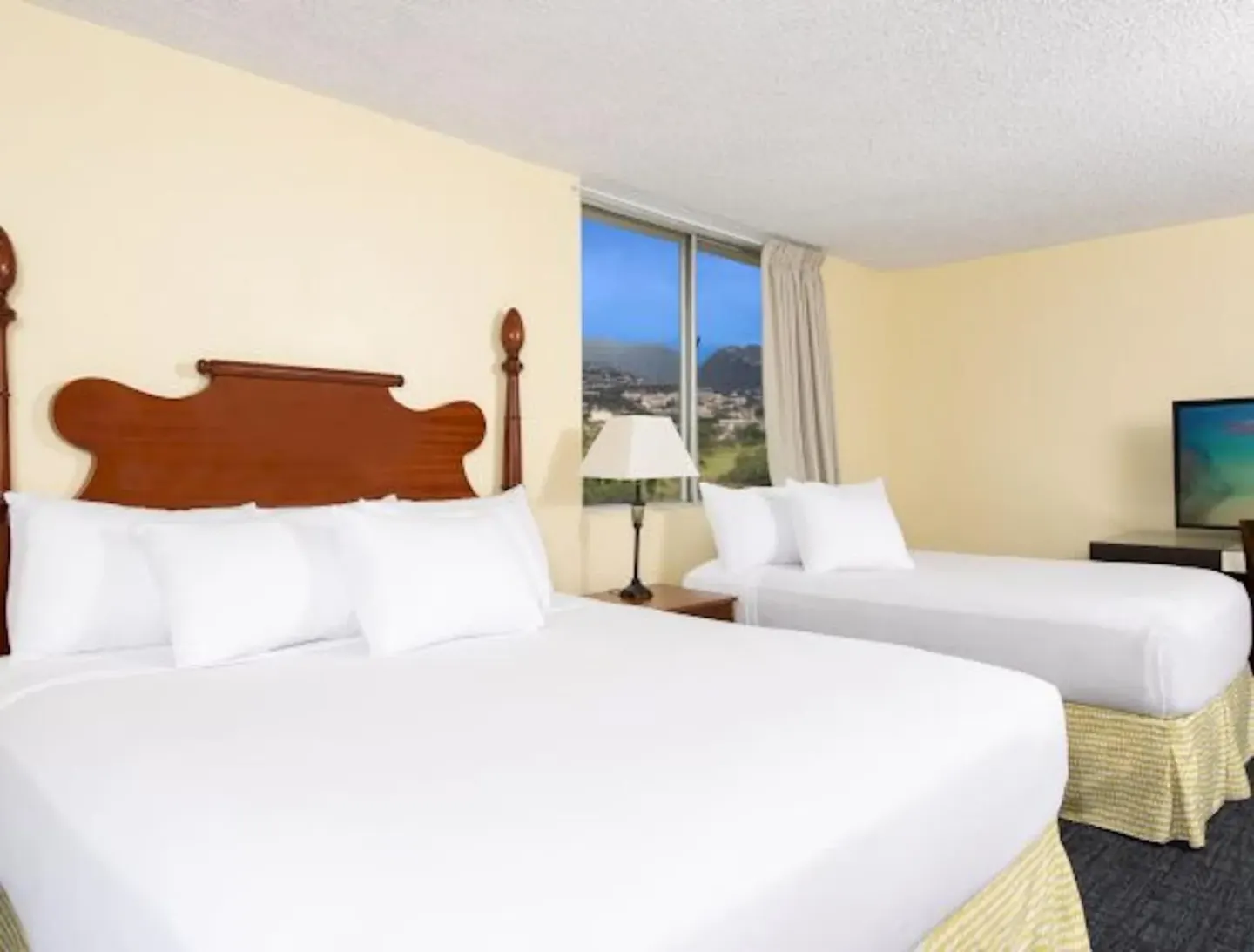 Guest room with two white beds and a window view at Ohia Waikiki Studio Suites.