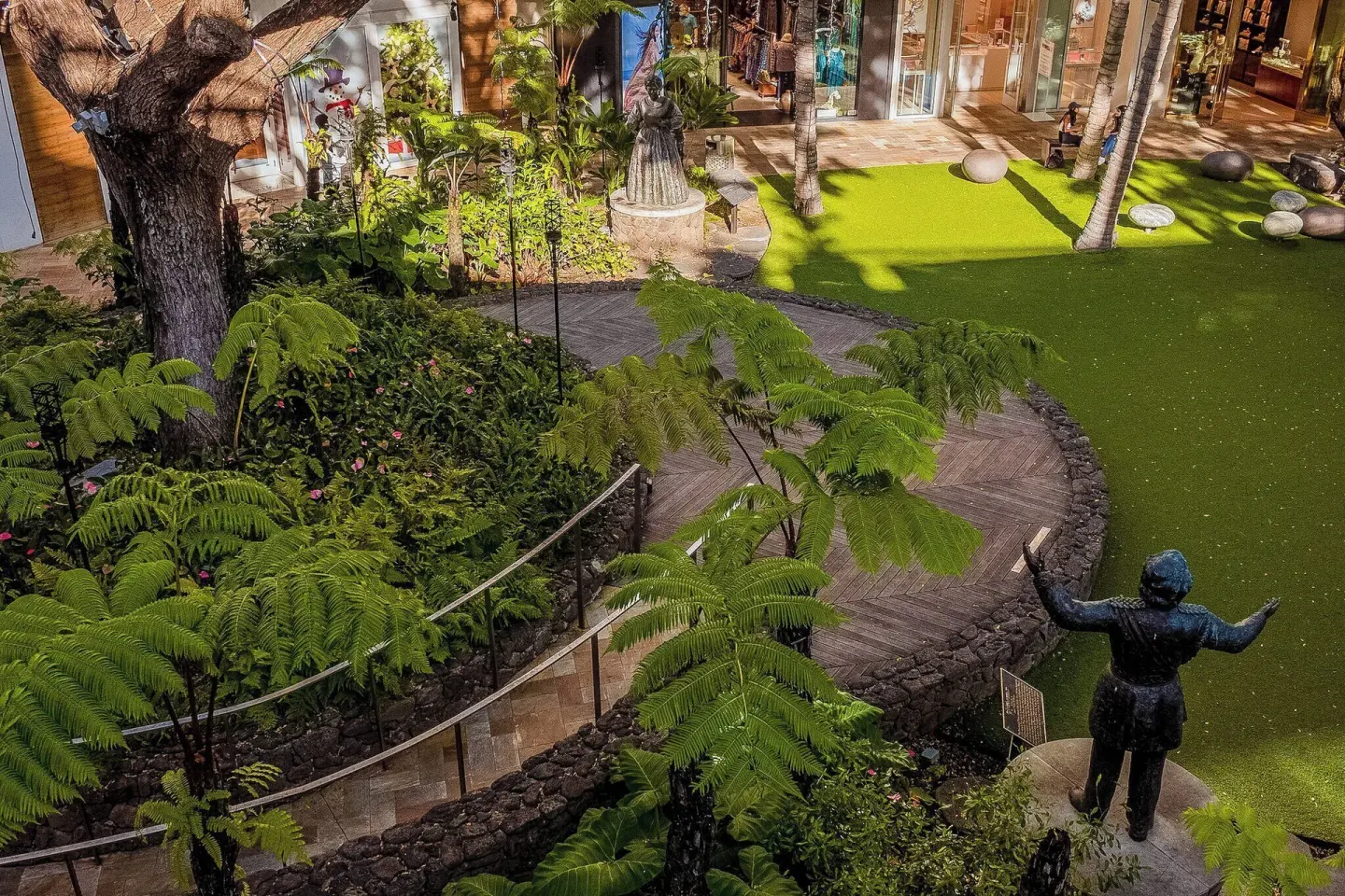 Landscaped walkway with palms, statues, and storefronts near Ohia Waikiki Studio Suites.