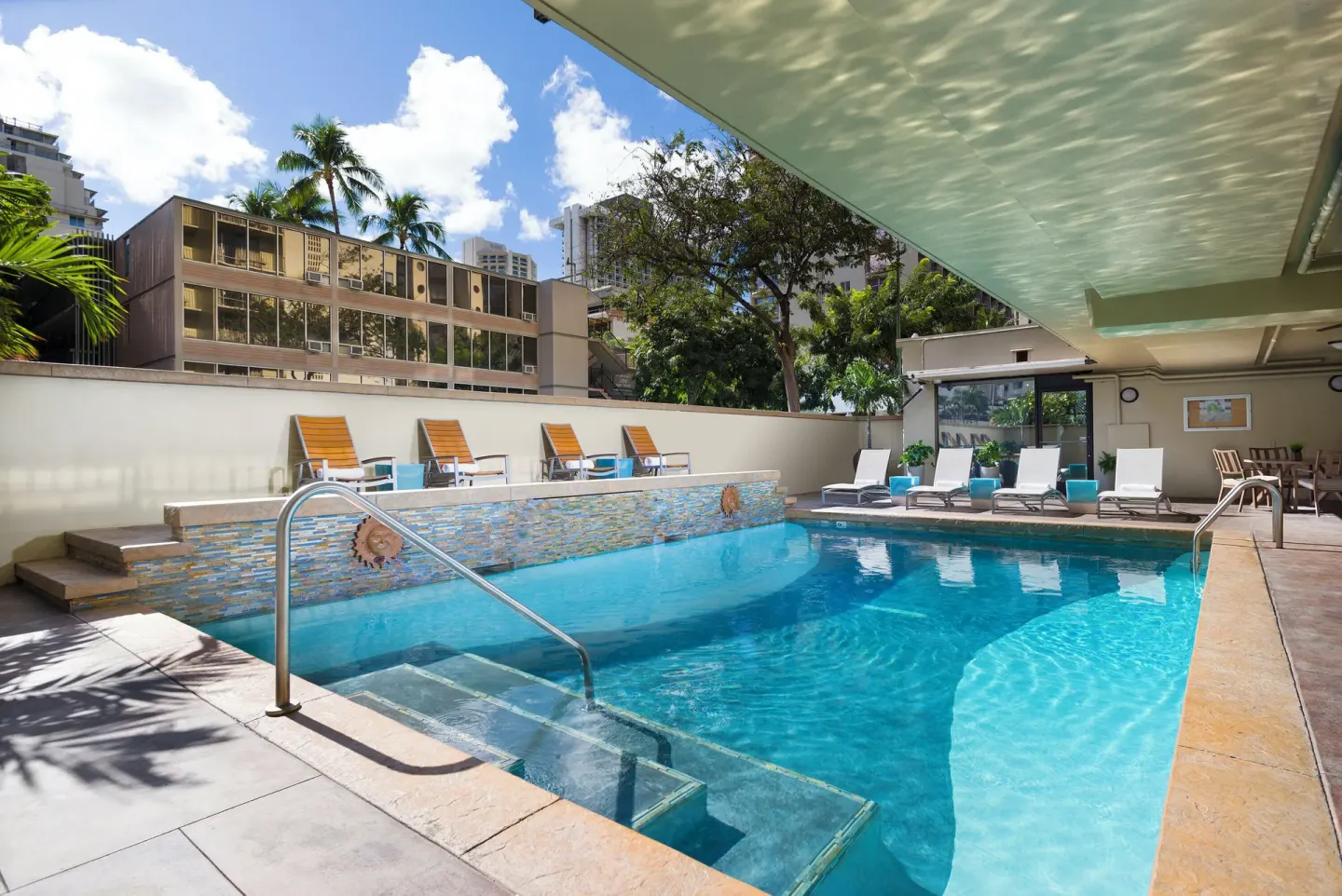 Outdoor pool with lounge chairs and city buildings at Ohia Waikiki Studio Suites.