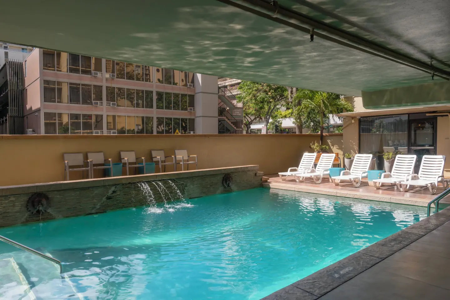Pool with lounge chairs and water features at Ohia Waikiki Studio Suites.