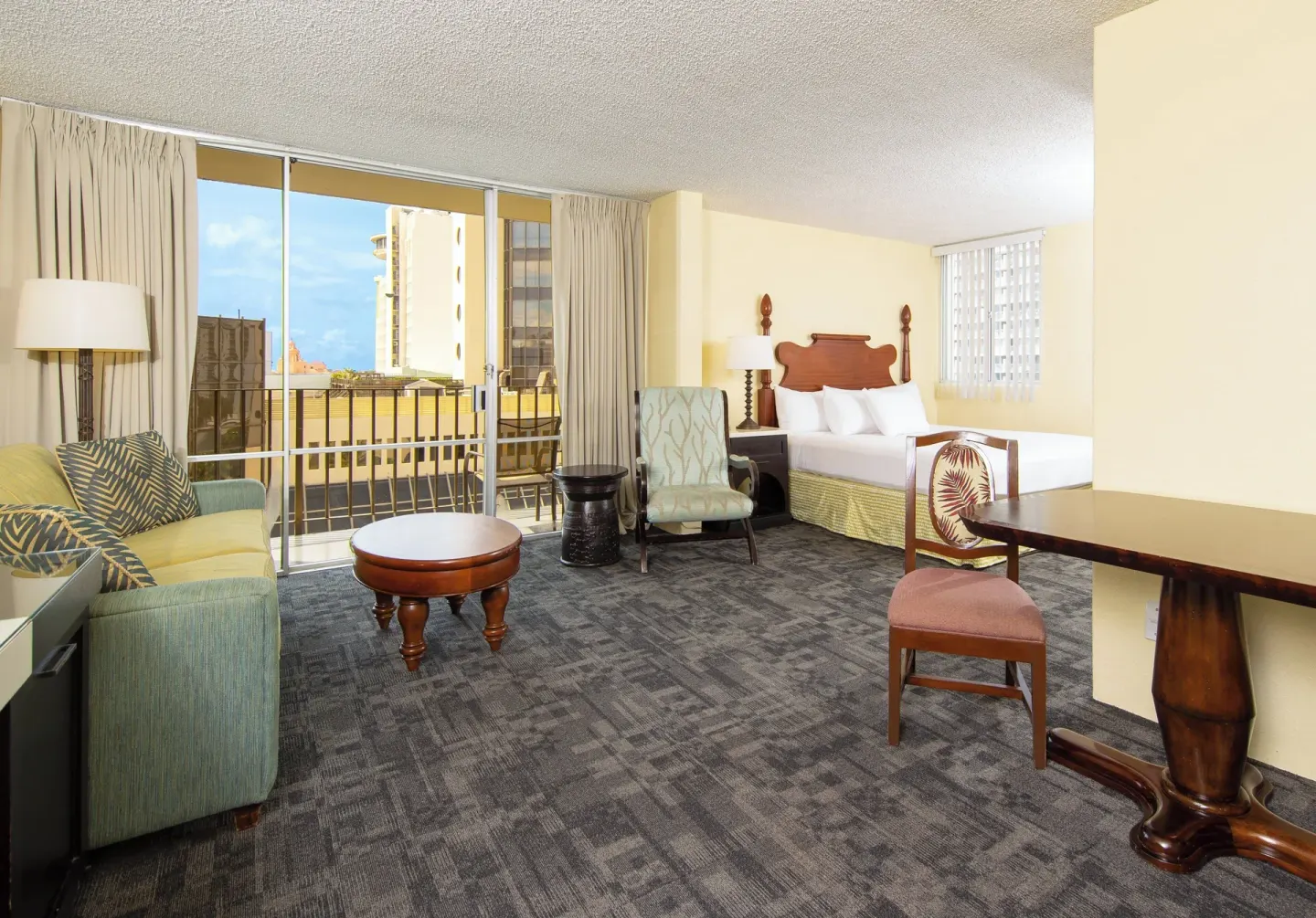 Suite with sitting area, dining table, bed, and balcony at Ohia Waikiki Studio Suites.